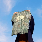 Person holding a camouflage shirt with 'JESUS' printed on it against a blue sky.